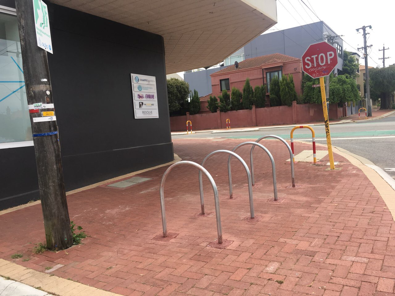 Bike Racks 2 Increase your business by investing in bike racks 1 Street view of bike racks installed on a brick sidewalk near a building and a stop sign. Investing in bike racks increases business.