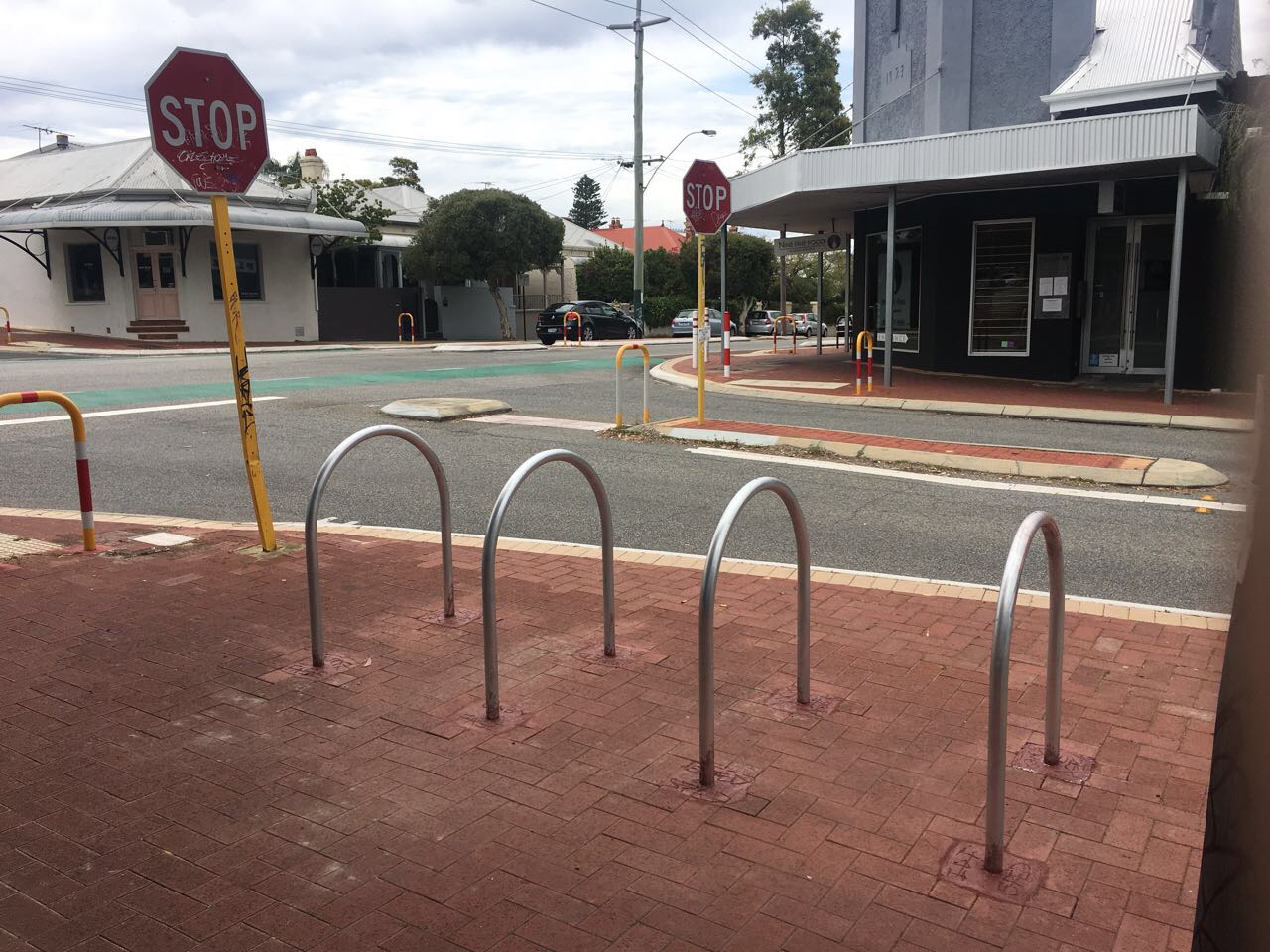 Bike Racks1 4 Tips for Locking Your Bike to Bike Racks 1 Bike racks on a brick sidewalk near a street intersection with stop signs. Tips for locking your bike to bike racks for security.