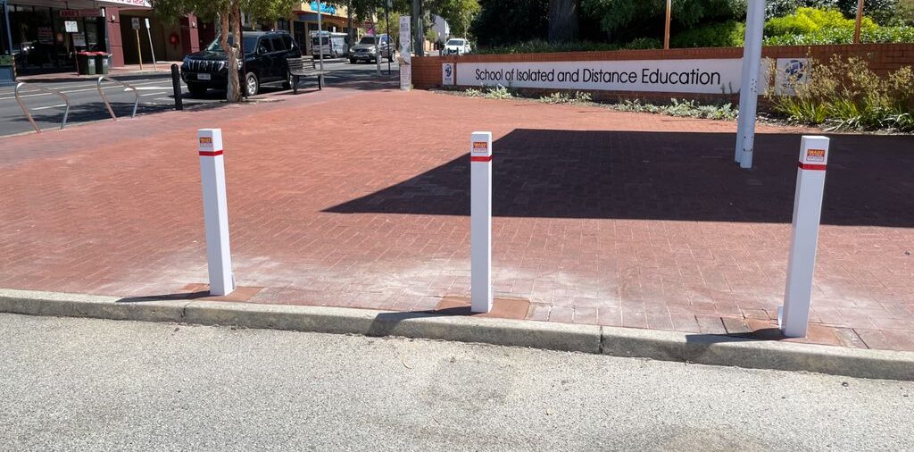 Removable Bollards Pic 2 1 e1709105795539 Home Page 74 Dugite 90mm x 900mm Padlockable Removable Bollard Square White, featuring three white bollards with red accents, standing on a brick-paved area.