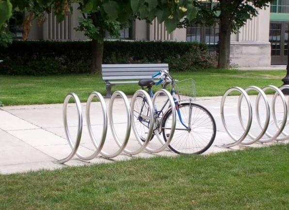 Perth Bike Parking: A blue bicycle secured in a modern, circular metal bike rack on a sidewalk next to green grass and a bench.