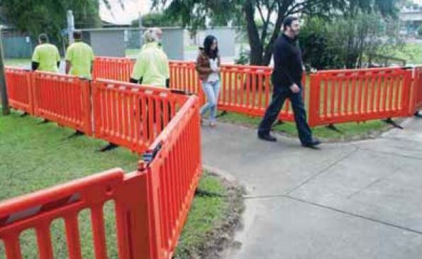 People walking by orange crowd control barriers set up on grass and a sidewalk. Crowd control tips shown.
